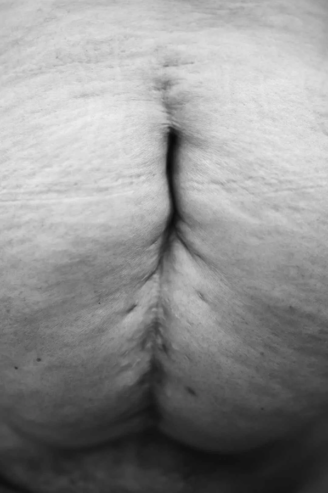 Close-up black and white photograph of a person's buttocks with the cleft visible.
