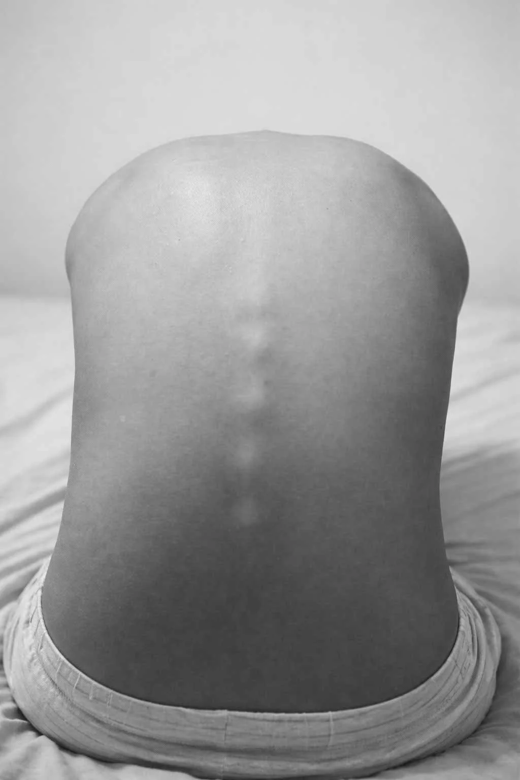 Close-up black and white photo of a person's lower back and buttocks, wearing light-colored shorts, with the focus on the shape of their back and posture.