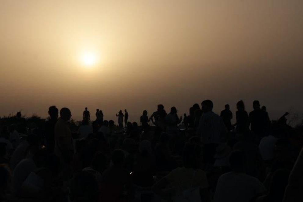 Silhouettes of people gathered outdoors against a hazy sunset sky.