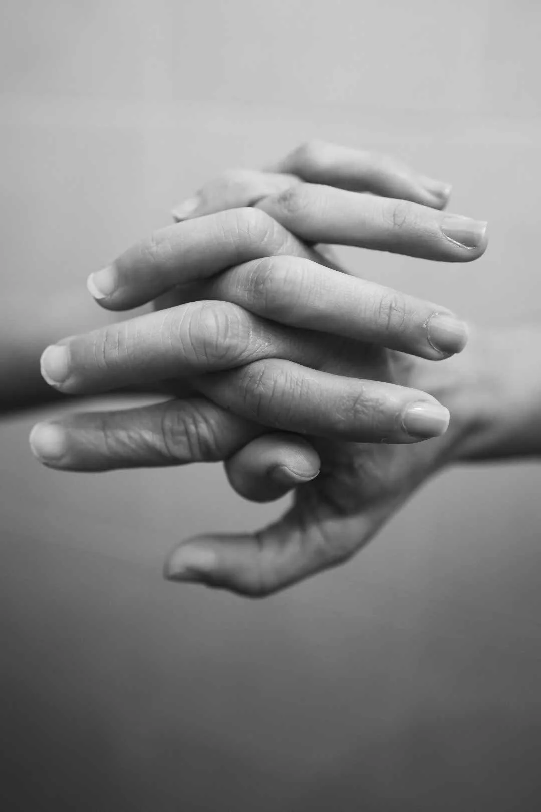 Black and white photo of two hands clasped together, with fingers intertwined, against a plain background.