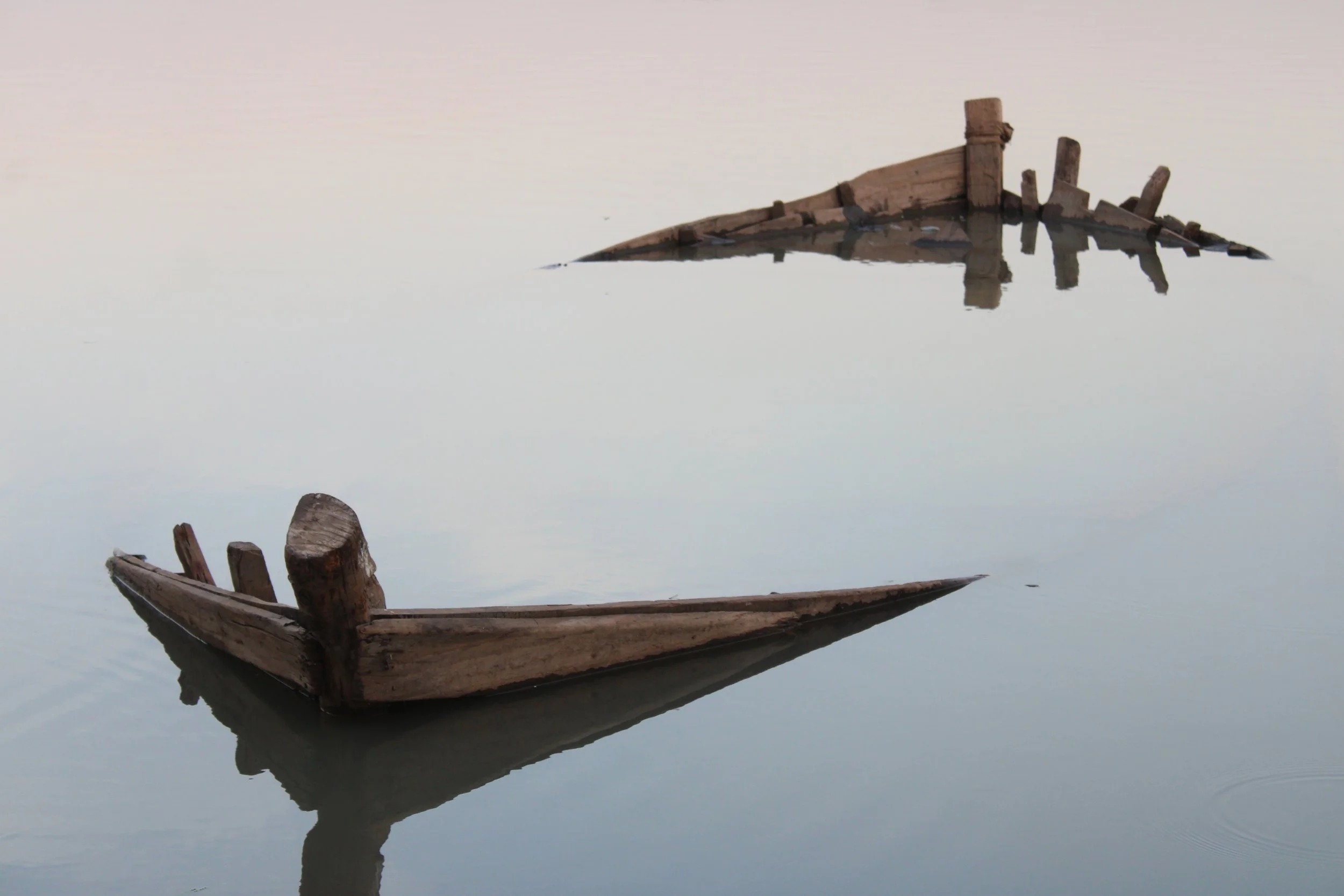 Two old wooden boats partially submerged in calm water with reflections.
