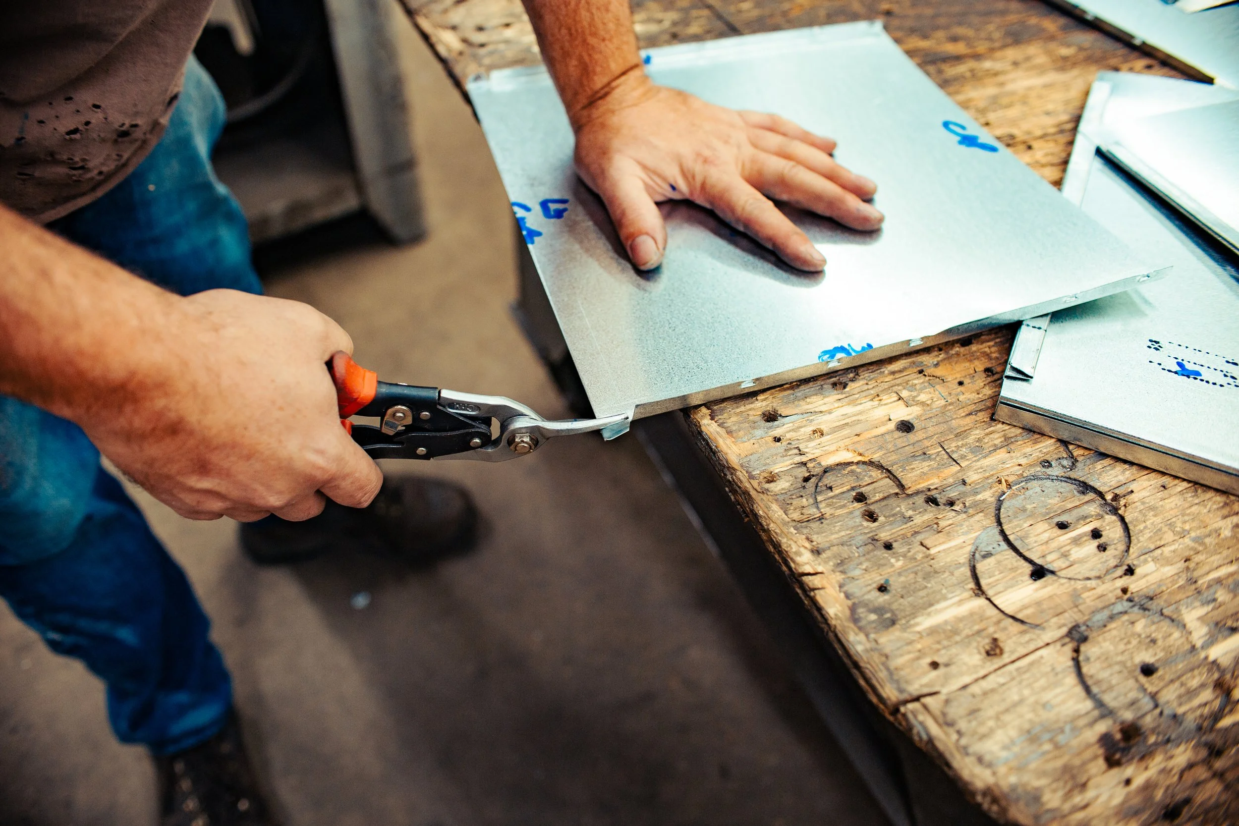 Person using tin snips to cut sheet metal on a wooden workbench.