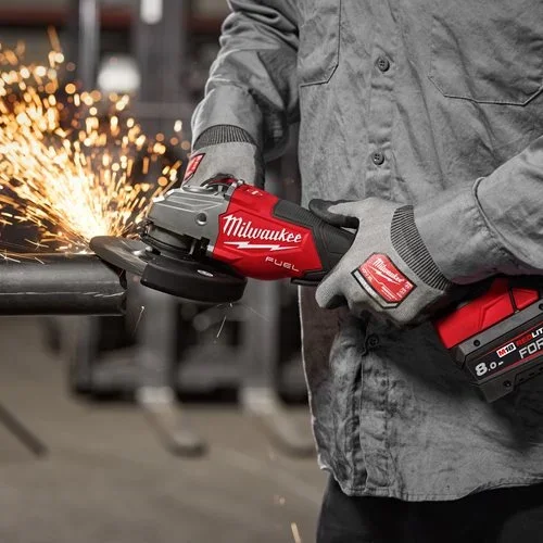 Person wearing gray work clothes and gloves using a red Milwaukee angle grinder to cut metal, with sparks flying.