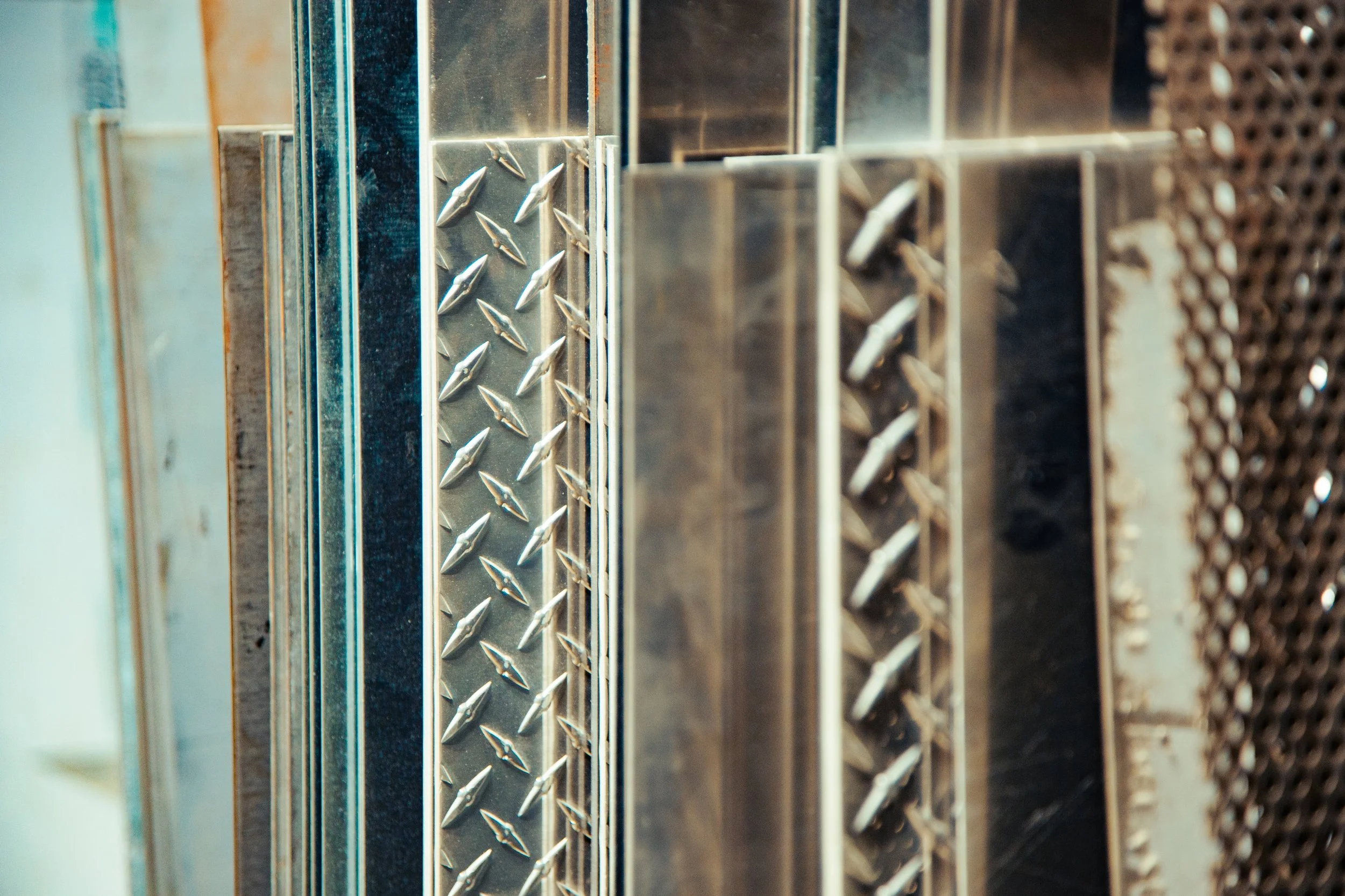 Close-up of various metal plates with different textures and patterns, including diamond plate and perforated designs.