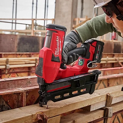 A person using a cordless Milwaukee power tool to cut wood on a construction site.