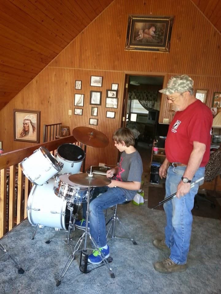 A young boy playing a drum set while an older man watches.