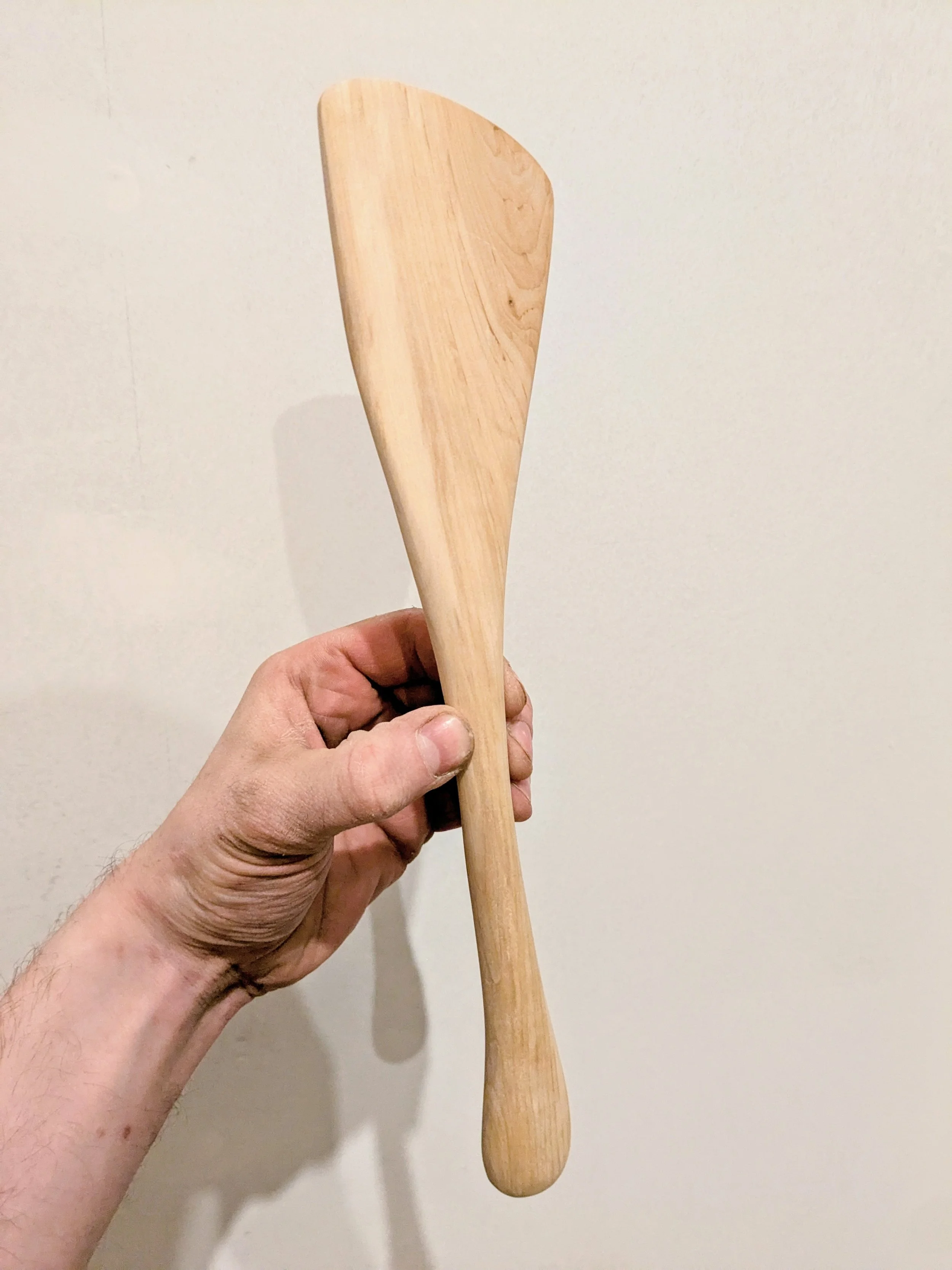 A person holding a wooden spatula against a plain off-white wall.