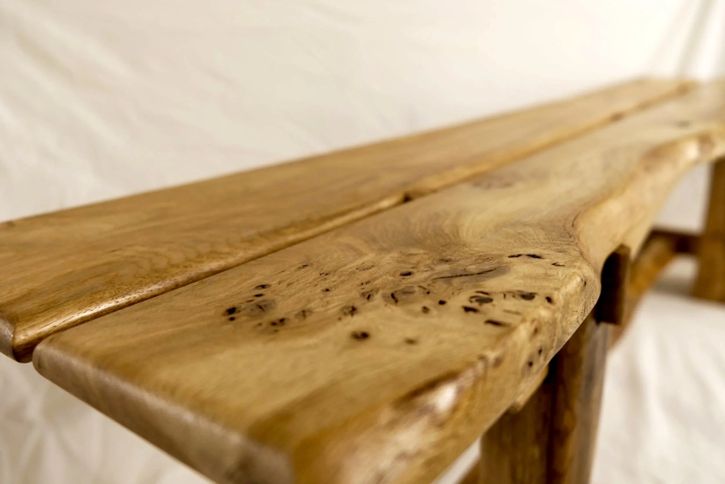 Close-up of a wooden table with a natural, uneven edge and visible wood grain, set against a neutral background.