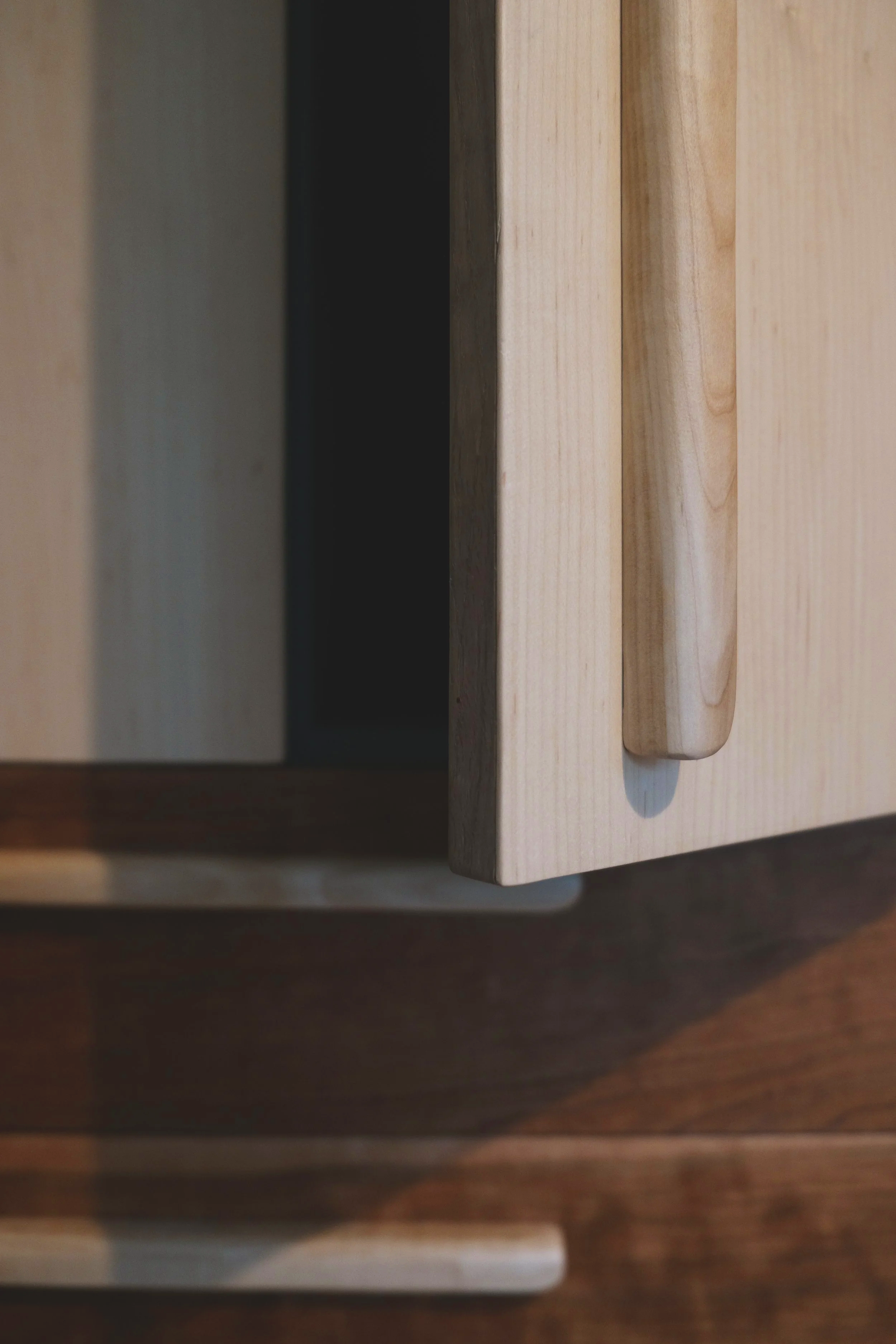 Close-up of a wooden cabinet with a handle, with shadows cast on the floor.