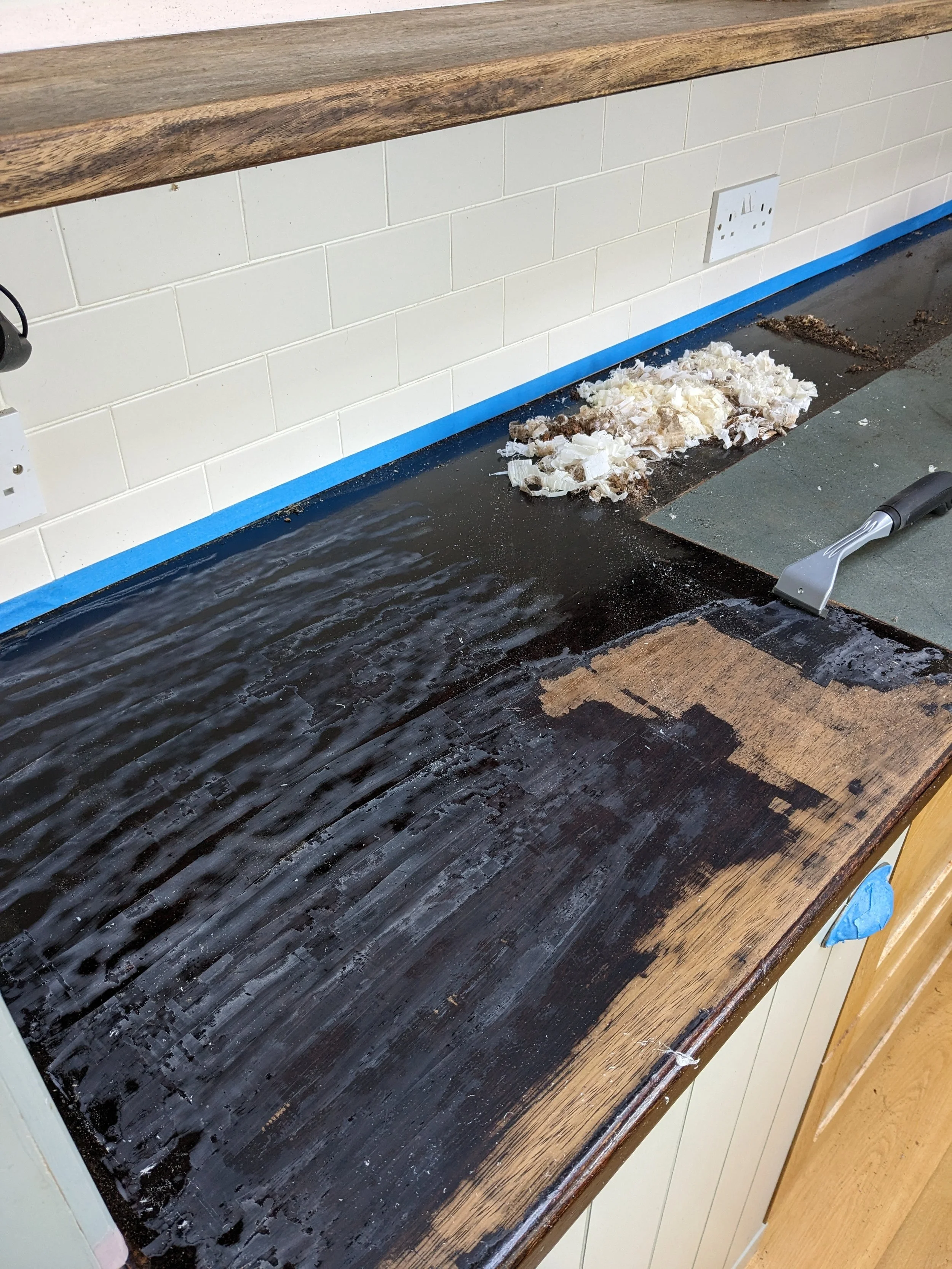 A kitchen countertop with a section cleaned and a section coated with a dark substance, a scraper tool, and peeled onions and debris on the countertop.