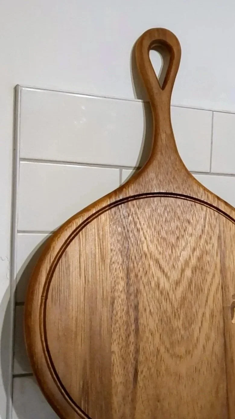 A wooden cutting board with a handle hanging on a wall.