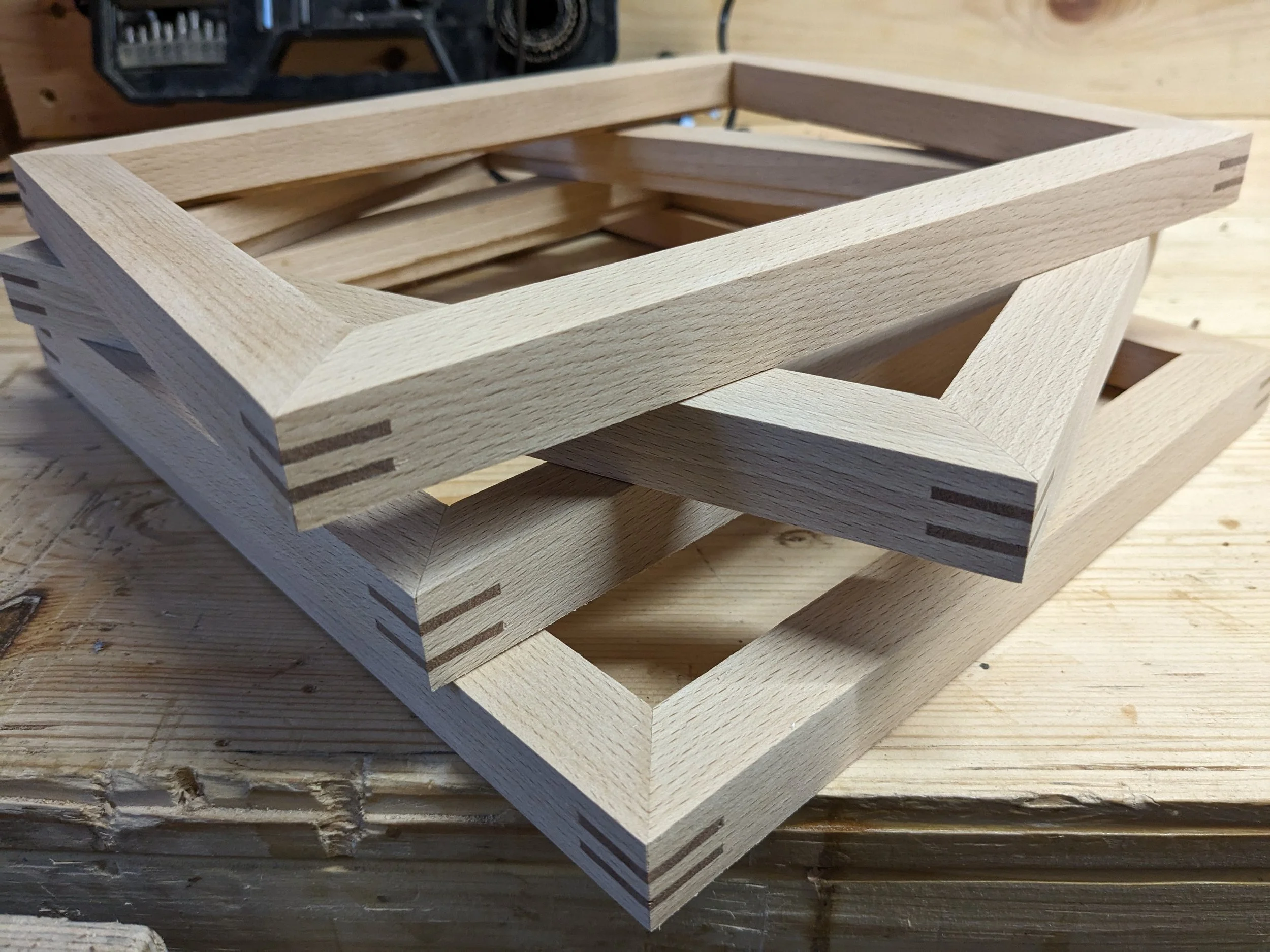 Stacked wooden picture frames on a workbench in a woodworking shop.