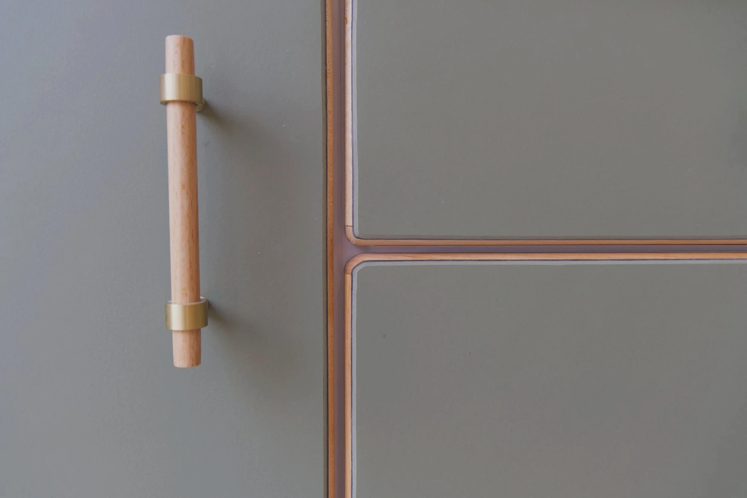 Close-up of a modern, minimalist cabinet with a light green matte finish and a wooden handle with brass fittings.