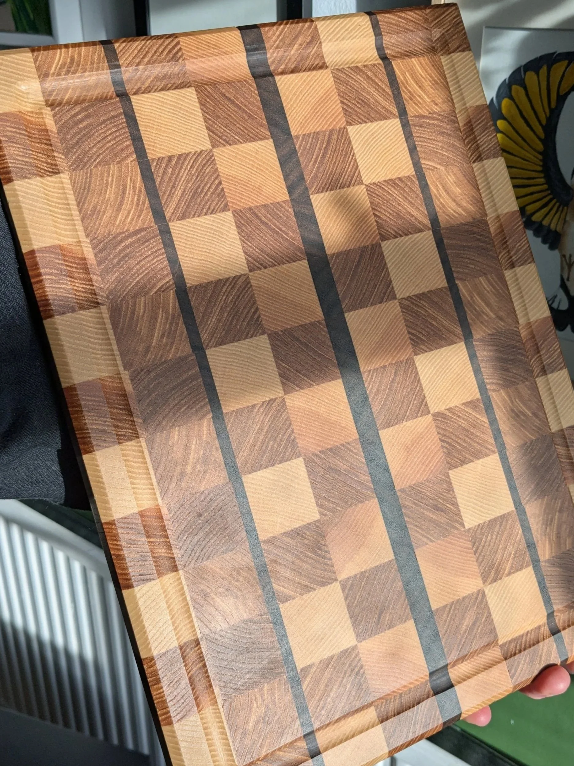 A wooden chessboard with alternating light and dark wood squares, bordered by a frame of similar wood, featuring vertical black lines dividing the board into sections.
