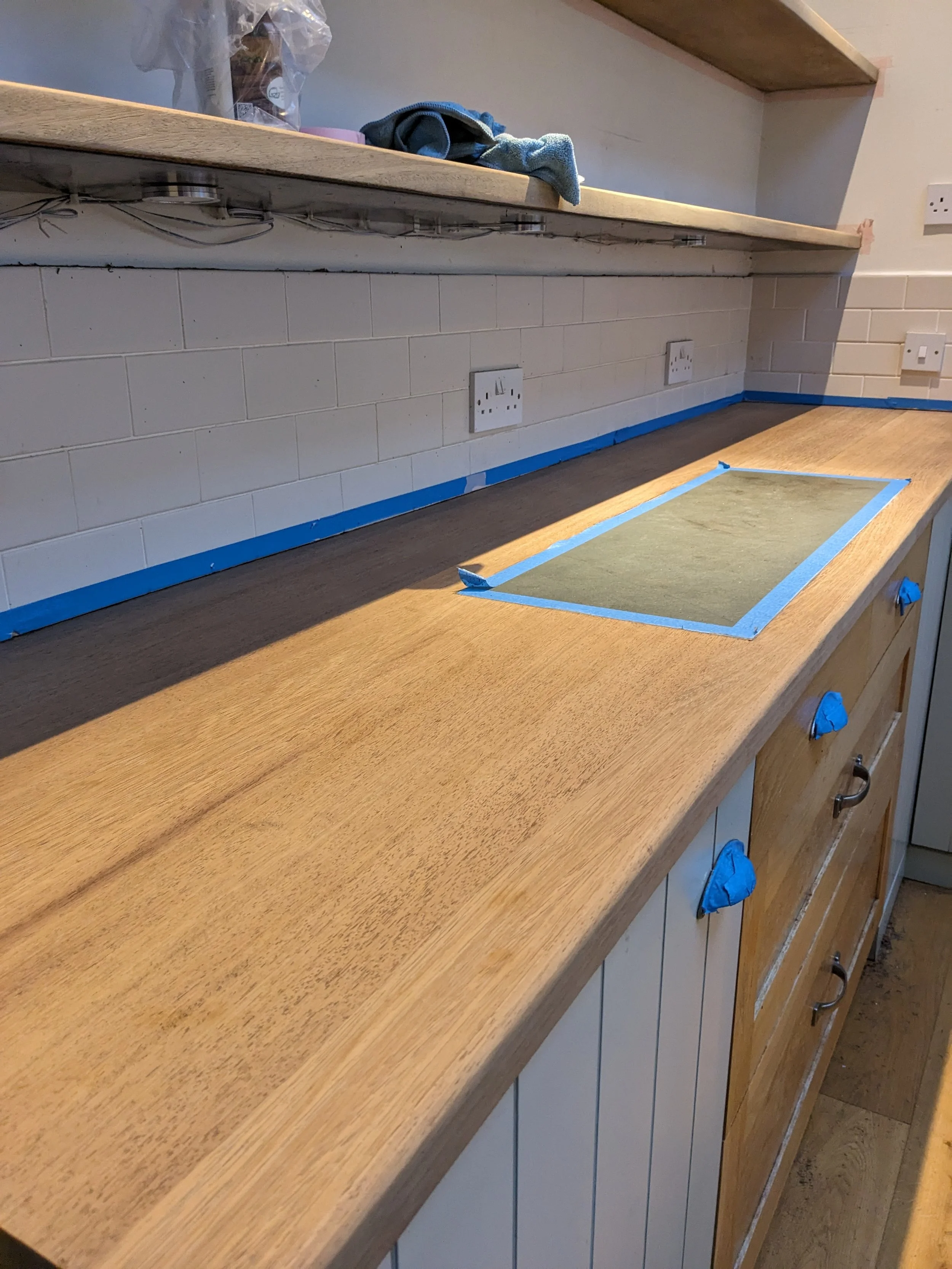Kitchen countertop with blue painter's tape marking a rectangular area, existing cabinetry, electrical outlets, and a tiled backsplash.