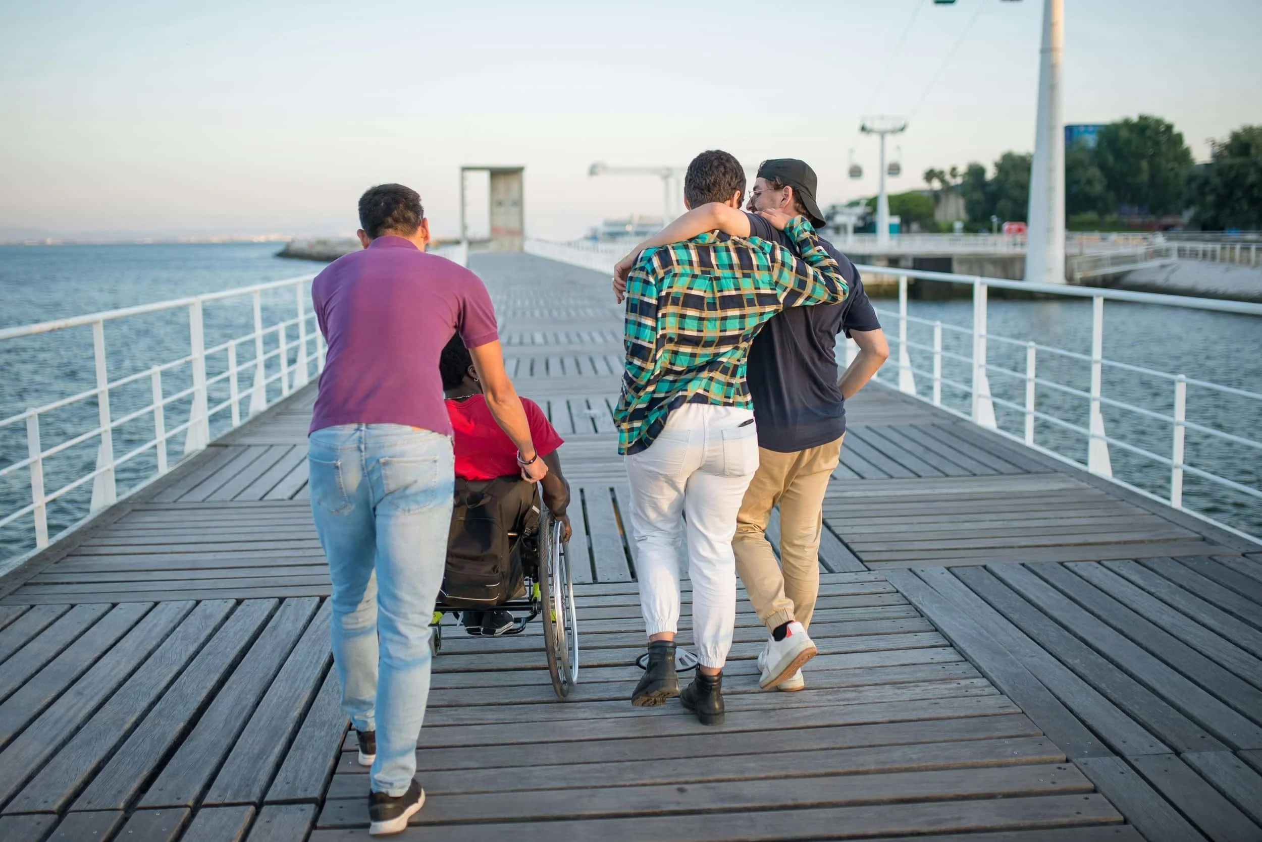 Friends walk on a boardwalk, one in a wheelchair, LGBTQ+ couple with arms around each other