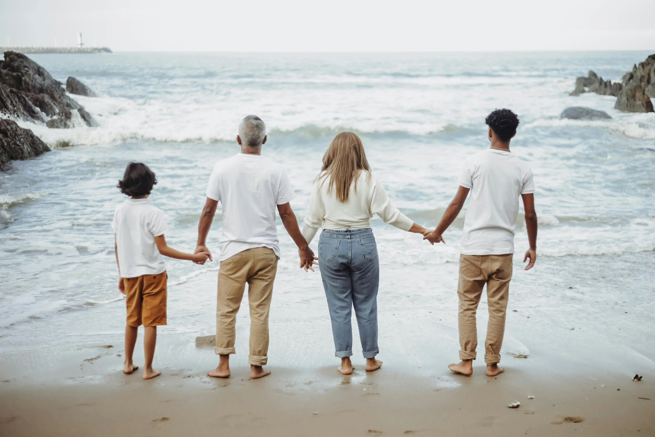 Grandparent, mom, teen, and boy hold hands on the beach in Hawaii