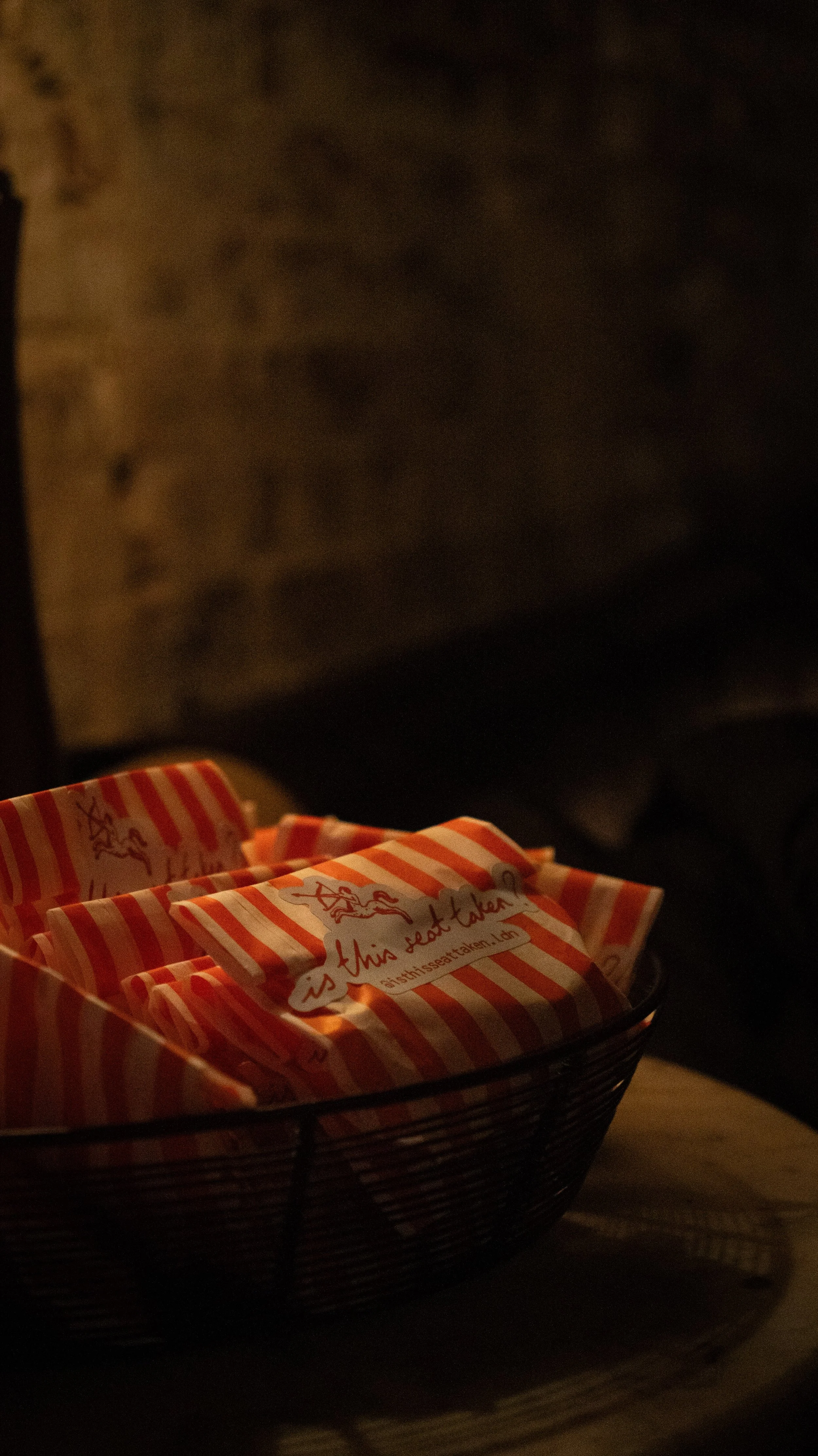 A black wire basket containing individually wrapped striped orange and white snacks with a logo and text, sitting on a wooden surface in a dimly lit setting.