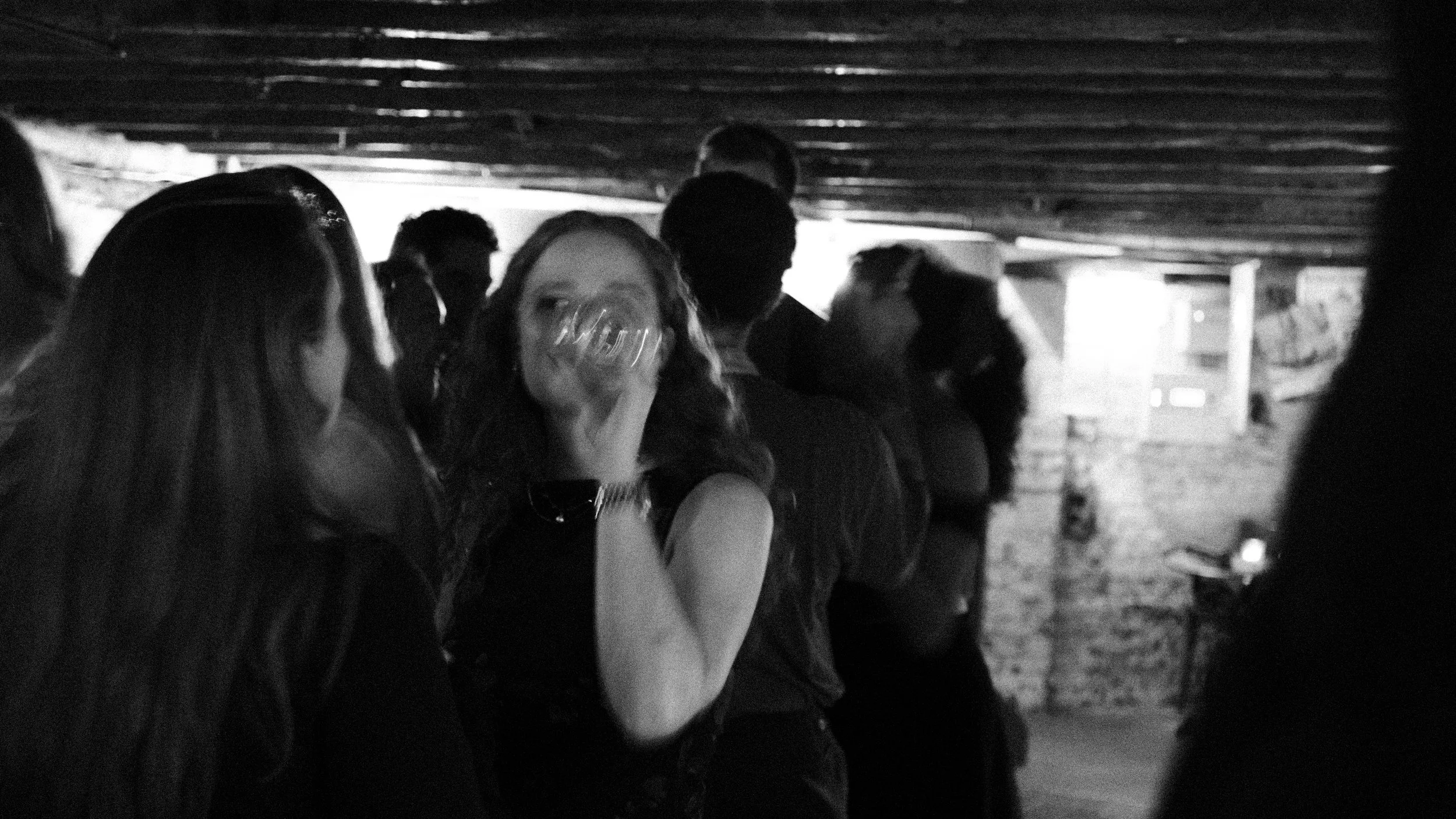 Group of people standing under a low ceiling, socializing at a party or gathering in black and white.