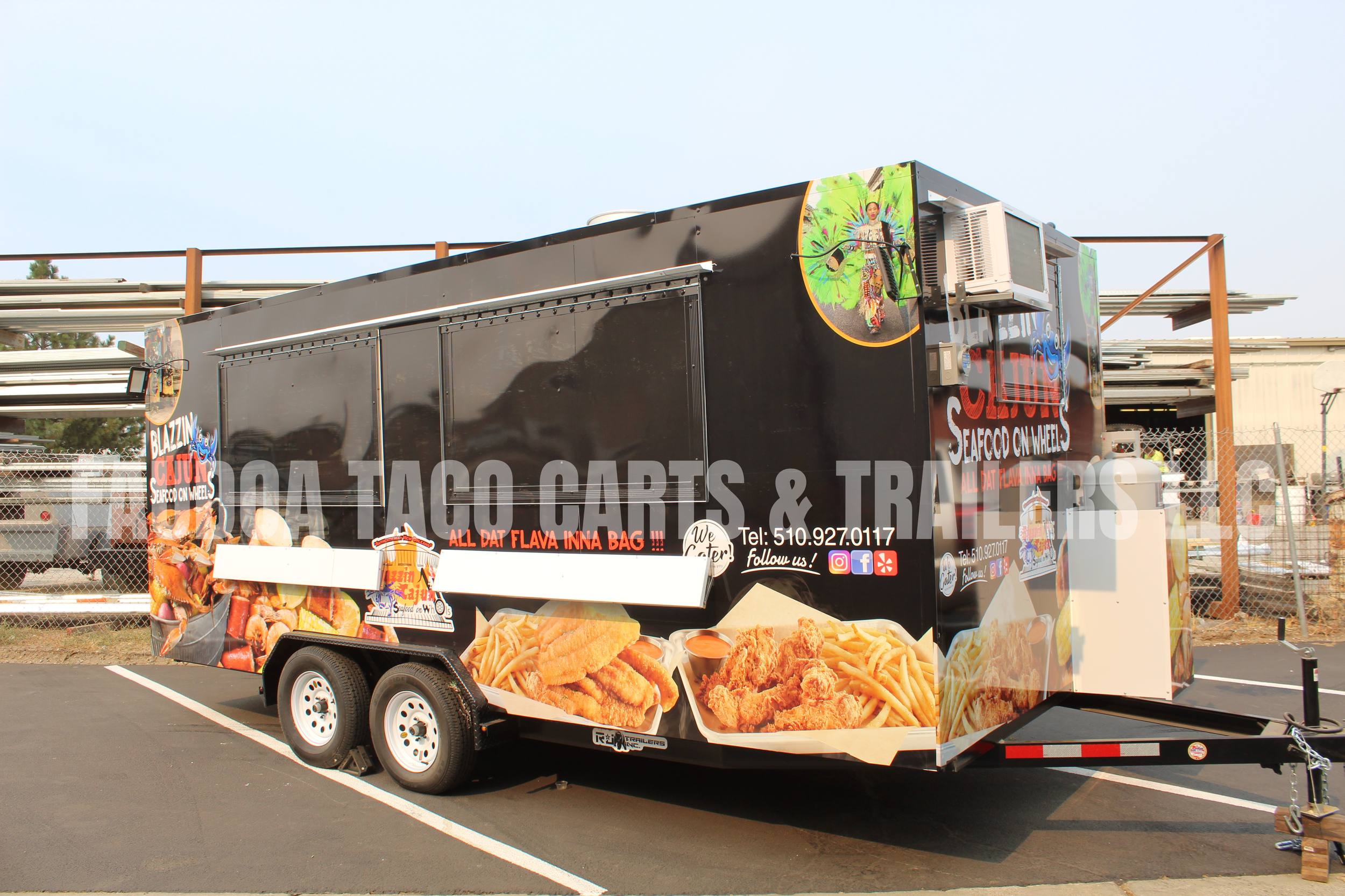 A black food trailer with large images of fried chicken and french fries, advertising seafood on wheels, parked in a lot with a chain-link fence in the background.