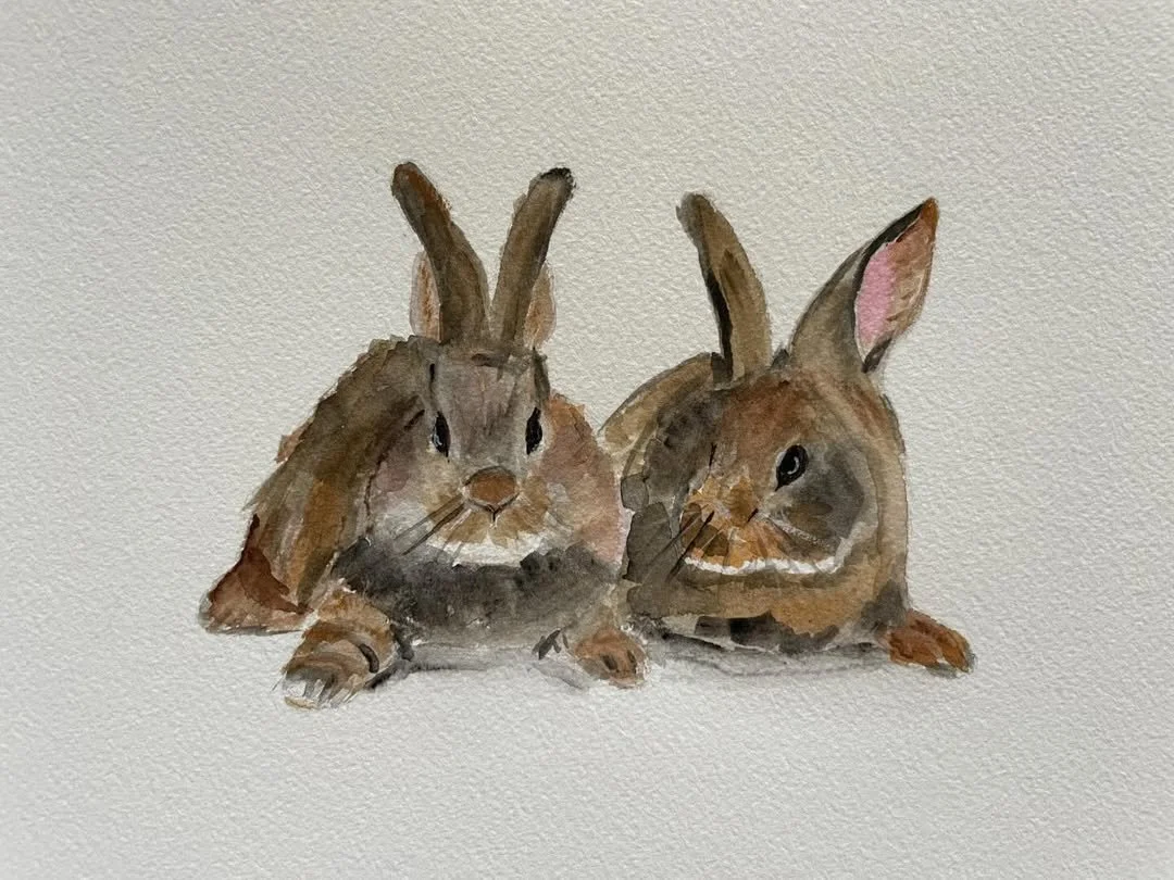 Watercolor painting of two brown rabbits sitting on a white background, one facing forward, the other in profile.