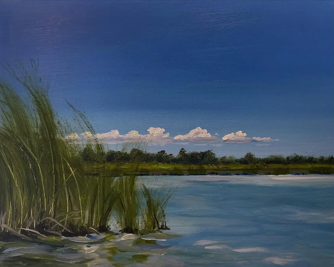A landscape painting of a river with tall green grass in the foreground, a line of trees in the background, and a clear blue sky with some white clouds.