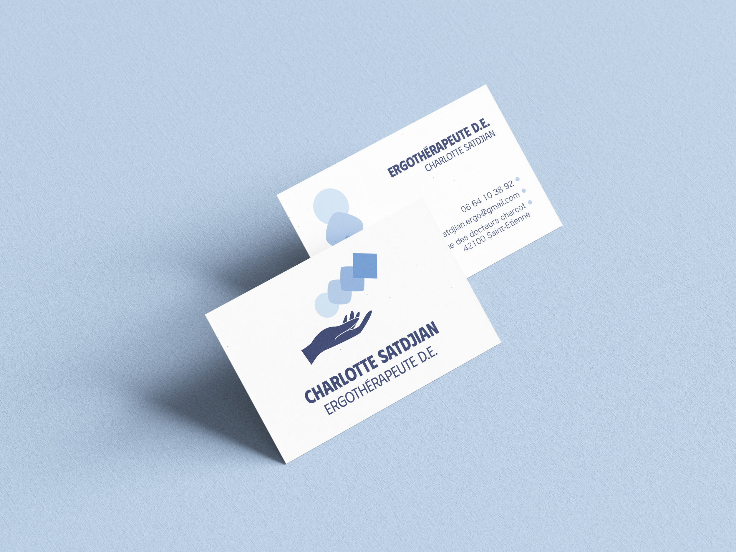 Deux cartes de visite pliées avec le nom Charlotte Satdjan, ergothérapeute, une icône d'une main avec des formes géométriques au-dessus, et un fond bleu clair.