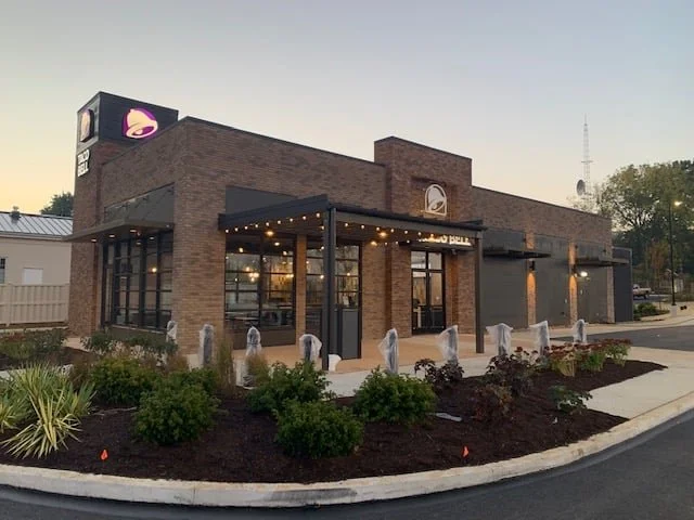 Exterior view of a Starbucks coffee shop with brick walls, large glass windows, a patio with string lights, and the Starbucks logo on the building and sign.