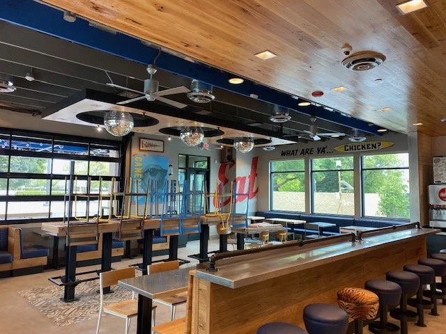 Interior of a closed restaurant with empty tables and chairs, large windows, and disco balls hanging from the ceiling.