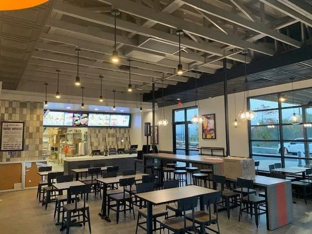 Empty modern cafe with black tables and chairs, pendant lighting, large windows, and digital menu boards.
