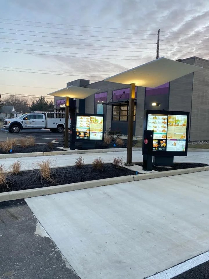 Fast food restaurant drive-thru with illuminated menu boards and modern design building in the background during early evening or late afternoon.