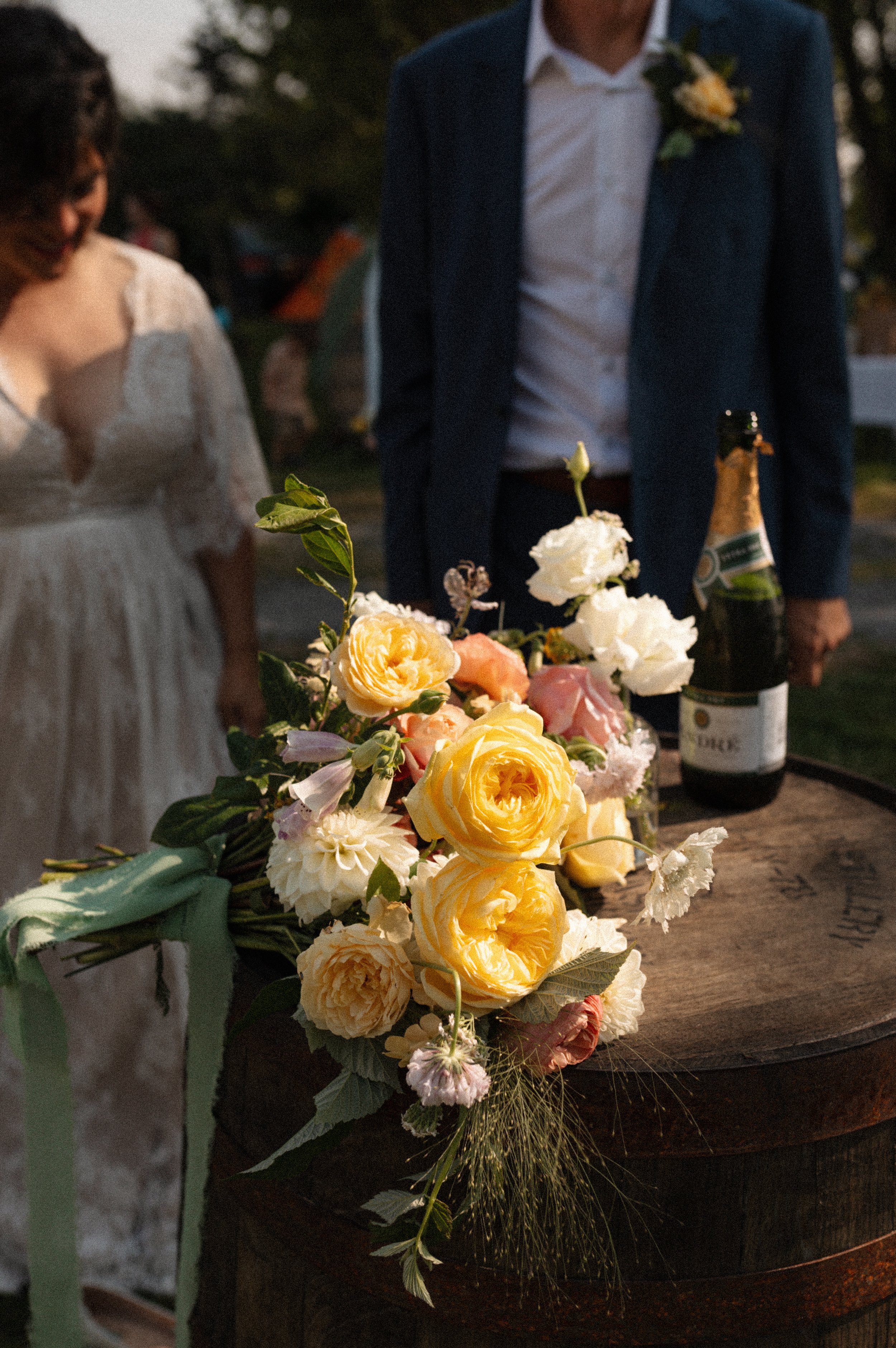 A floral arrangement with yellow and white flowers on a wooden barrel at an outdoor wedding.