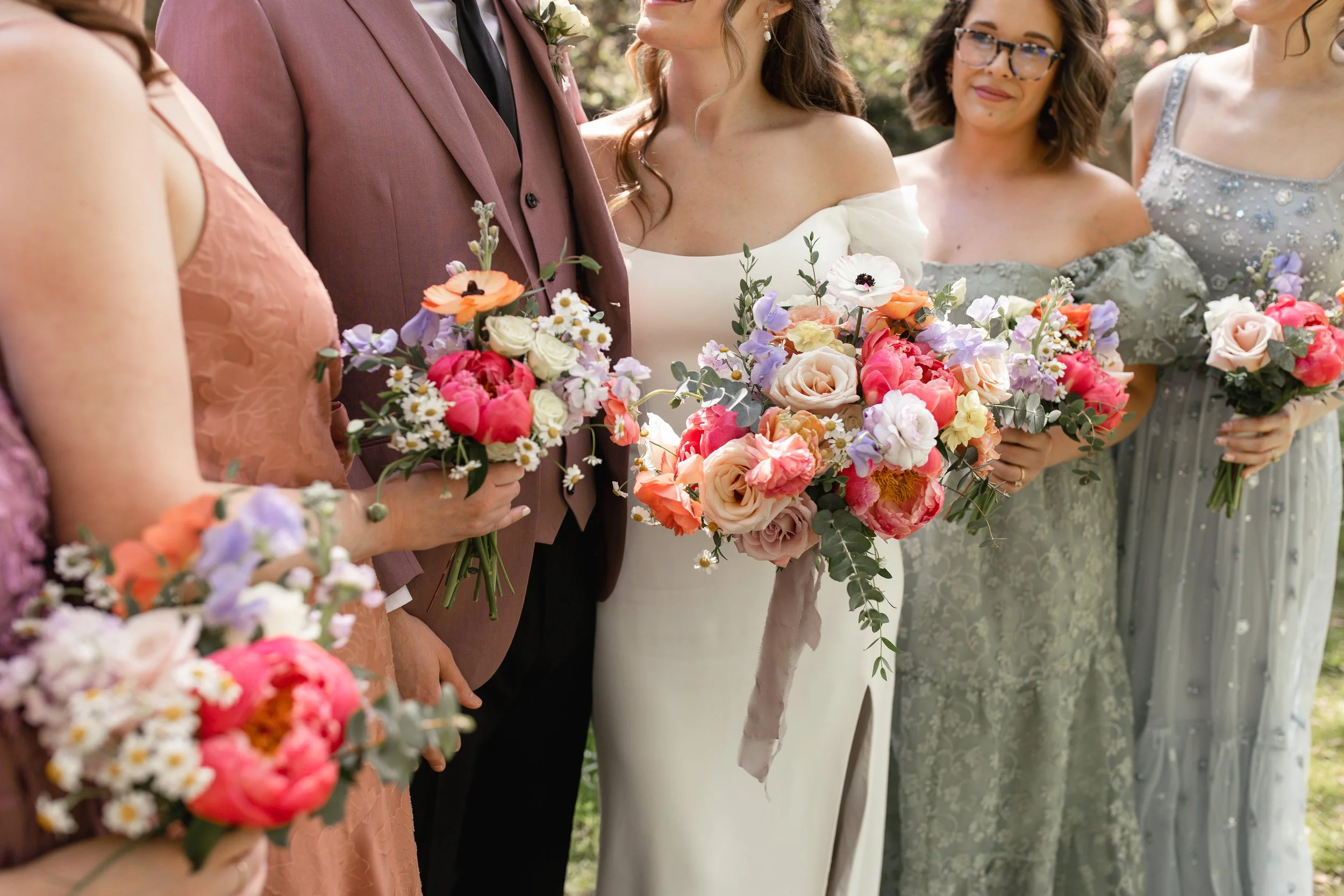 A woman's hand with an engagement ring resting on a light pink rose in a bouquet of white and blush pink flowers.