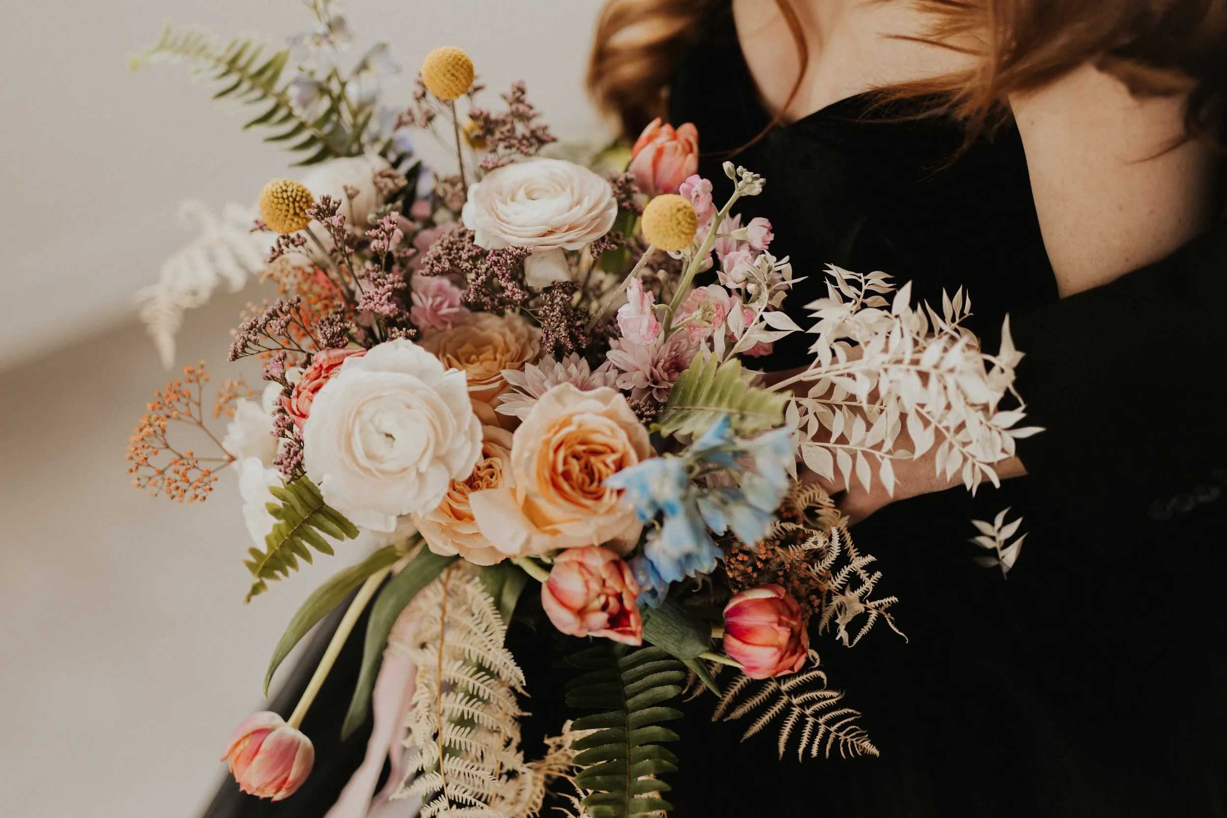 A person holding a colorful bouquet of flowers, including roses, tulips, and various foliage.