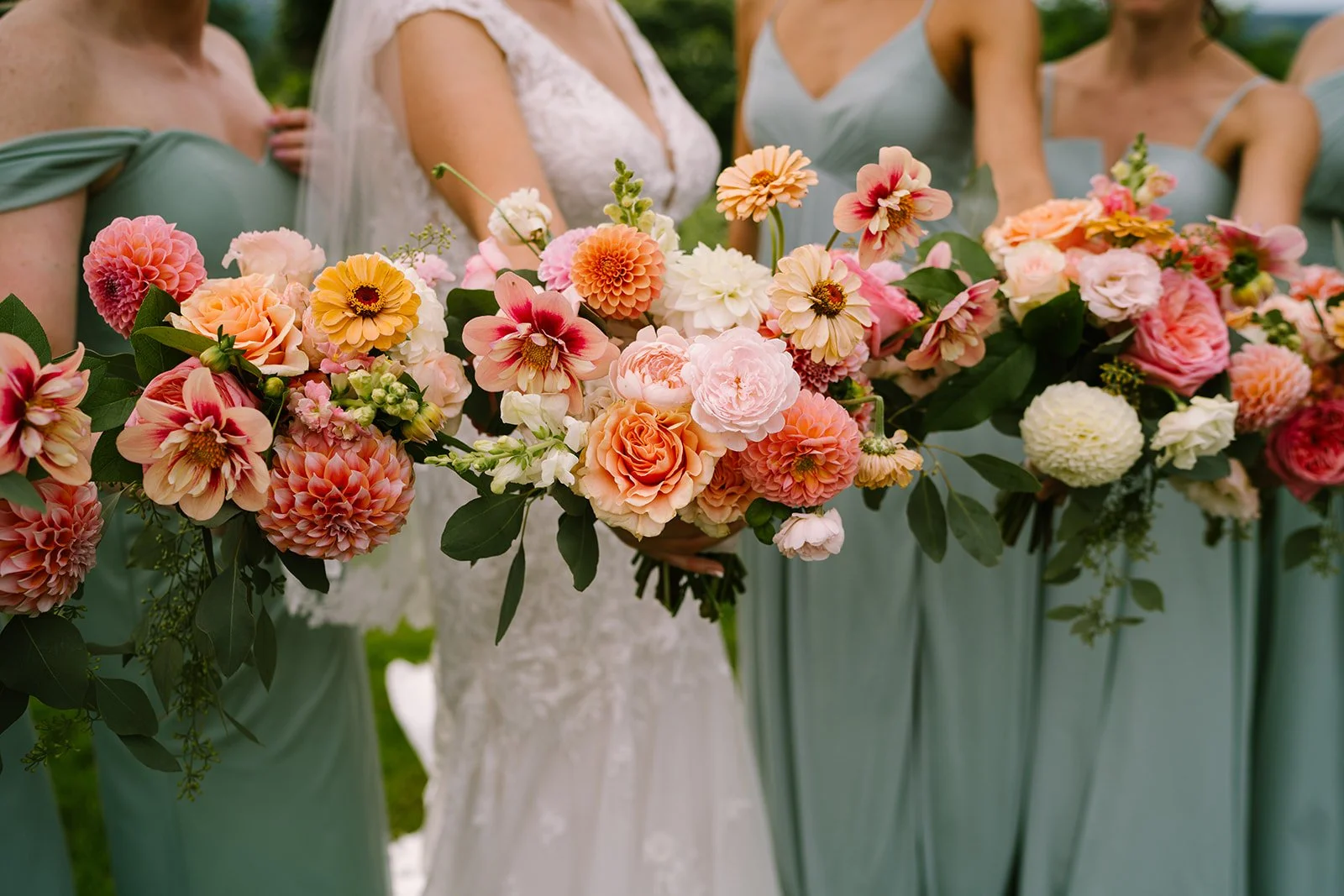 Bride and bridesmaids holding a large bouquet of pink, peach, and white flowers at a wedding.