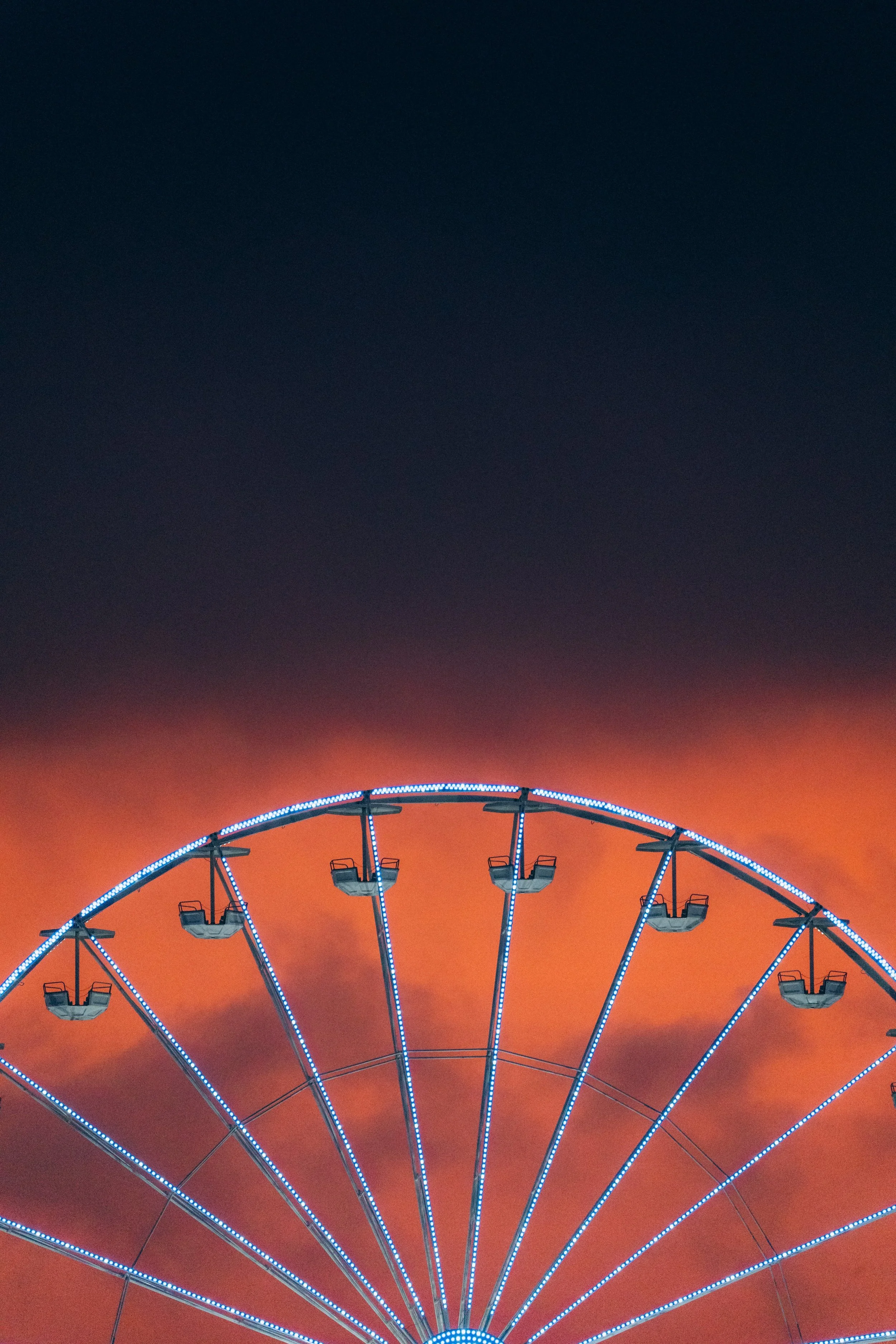 Grande roue illuminée avec des lumières bleues, contre un ciel au coucher du soleil avec des couleurs orange et rouge.