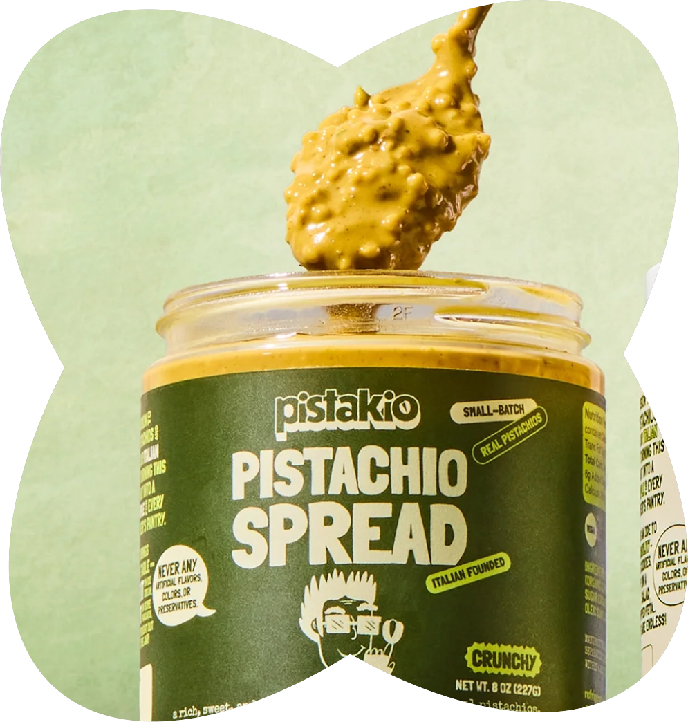 A spoonful of pistachio spread above a jar of pistachio spread with a green label, against a light green background.