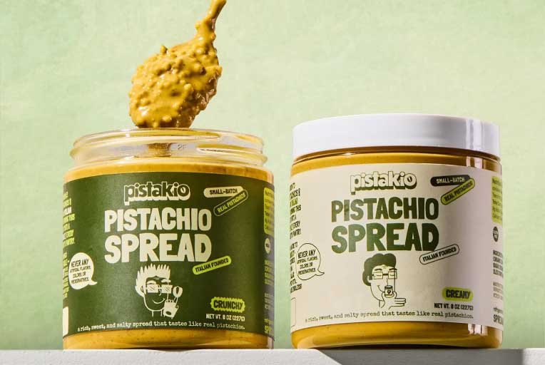 Two jars of Pistachio Spread on a light green background, one with a spoonful of spread above it.