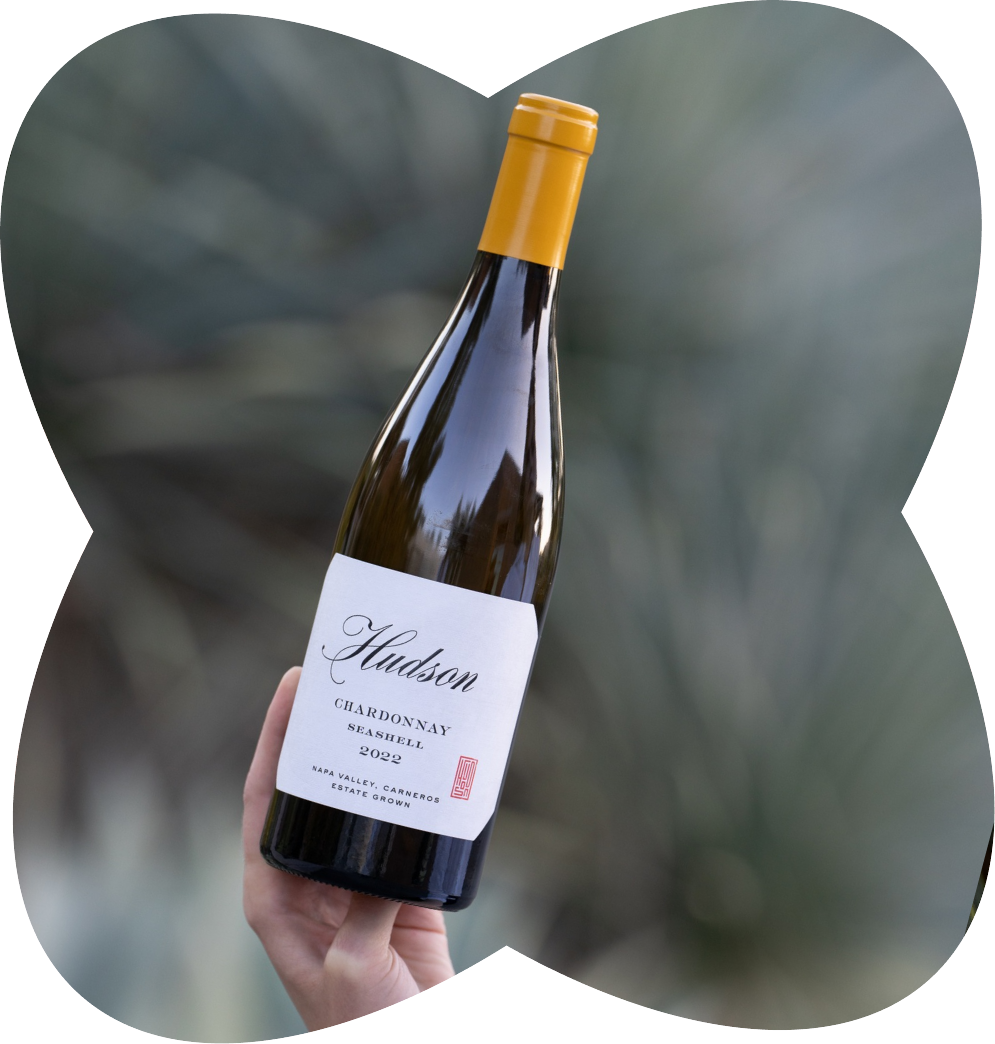 A hand holding a bottle of Hudson Chardonnay wine with a yellow cap, label indicating 2022 vintage, Napa Valley, California