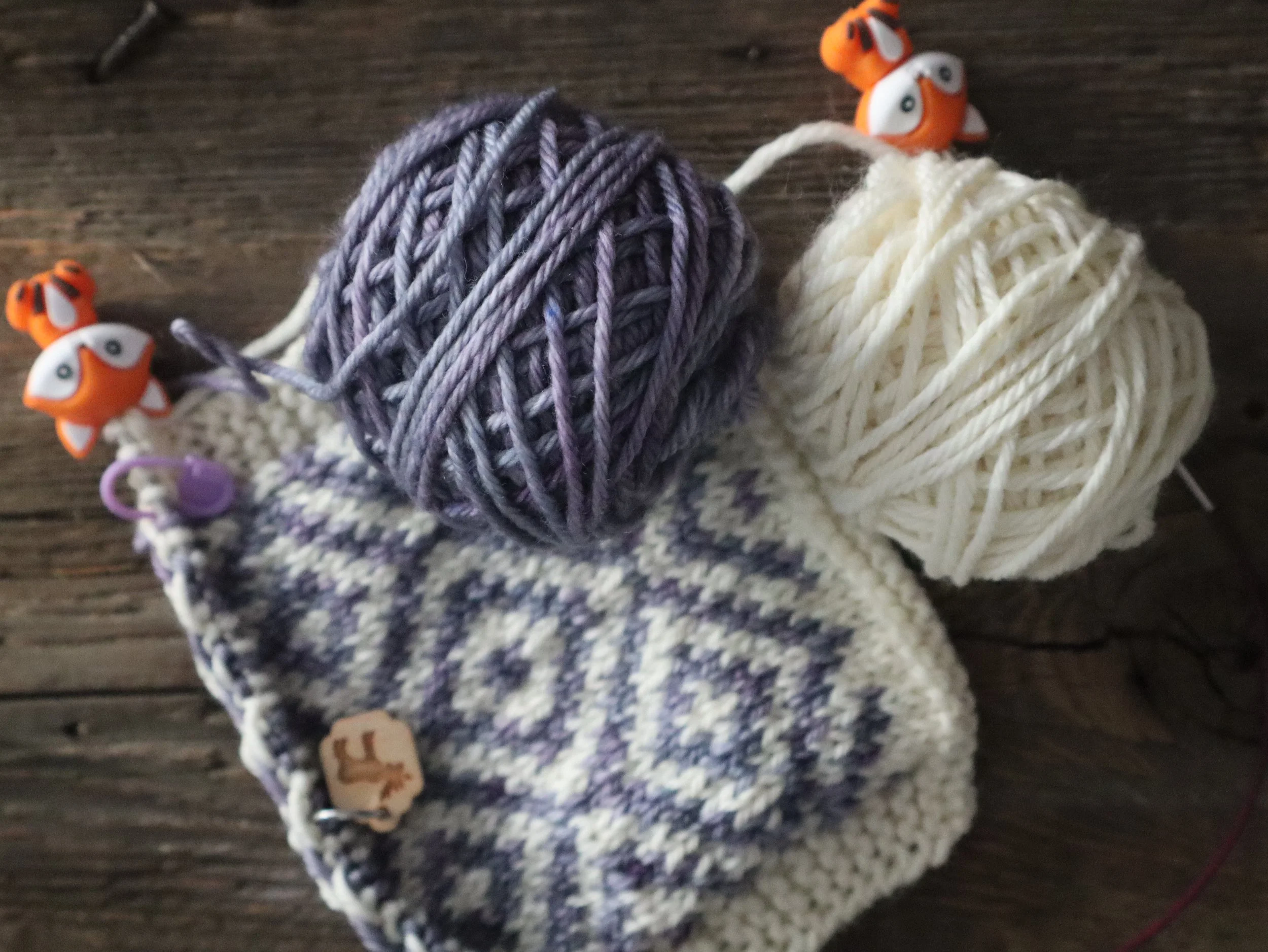 Purple and white colorwork knitting with fox needle stoppers.