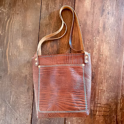 Brown leather shoulder bag with a front pocket, placed on a wooden surface.