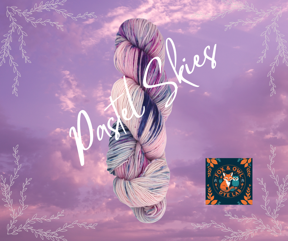 A skein of pastel-colored yarn with shades of pink, purple, blue, and white, set against a pink and purple sky with clouds. Decorative white leaf borders and text reading 'Pastel Skies', along with a logo for Fox & Owl Dye Lab.