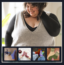 Woman with curly hair smiling, wearing a gray sweater over a black shirt, touching her hair.
