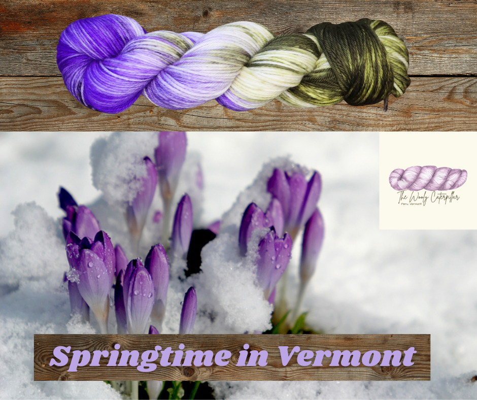 A skein of variegated purple, white, and green yarn placed on a wooden surface, with purple crocus flowers blooming in snow below and the text "Springtime in Vermont" on a wooden banner.