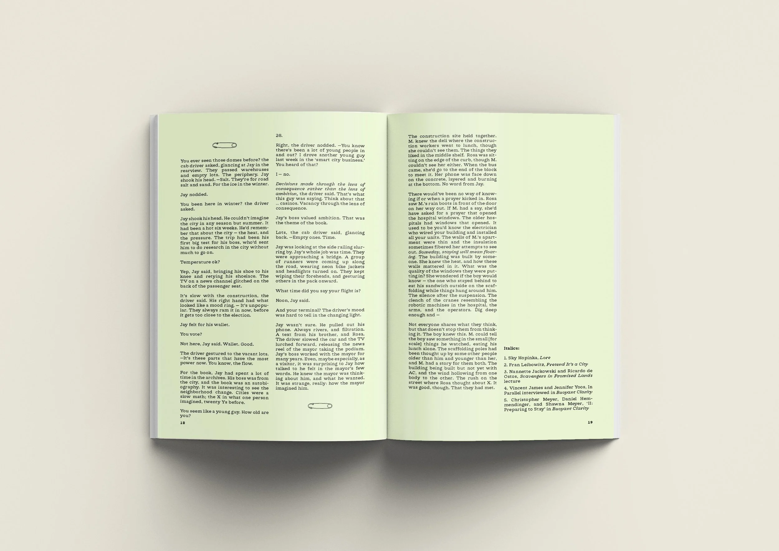 Open book with light green pages containing printed text in two columns and small decorative elements, laid on a beige surface.