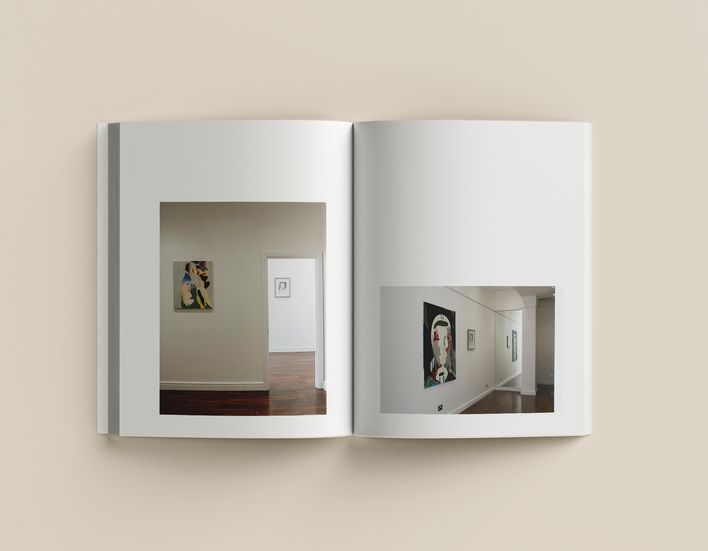 Open photo book showing interior photos of an art gallery with white walls and wooden floors, displaying abstract paintings.