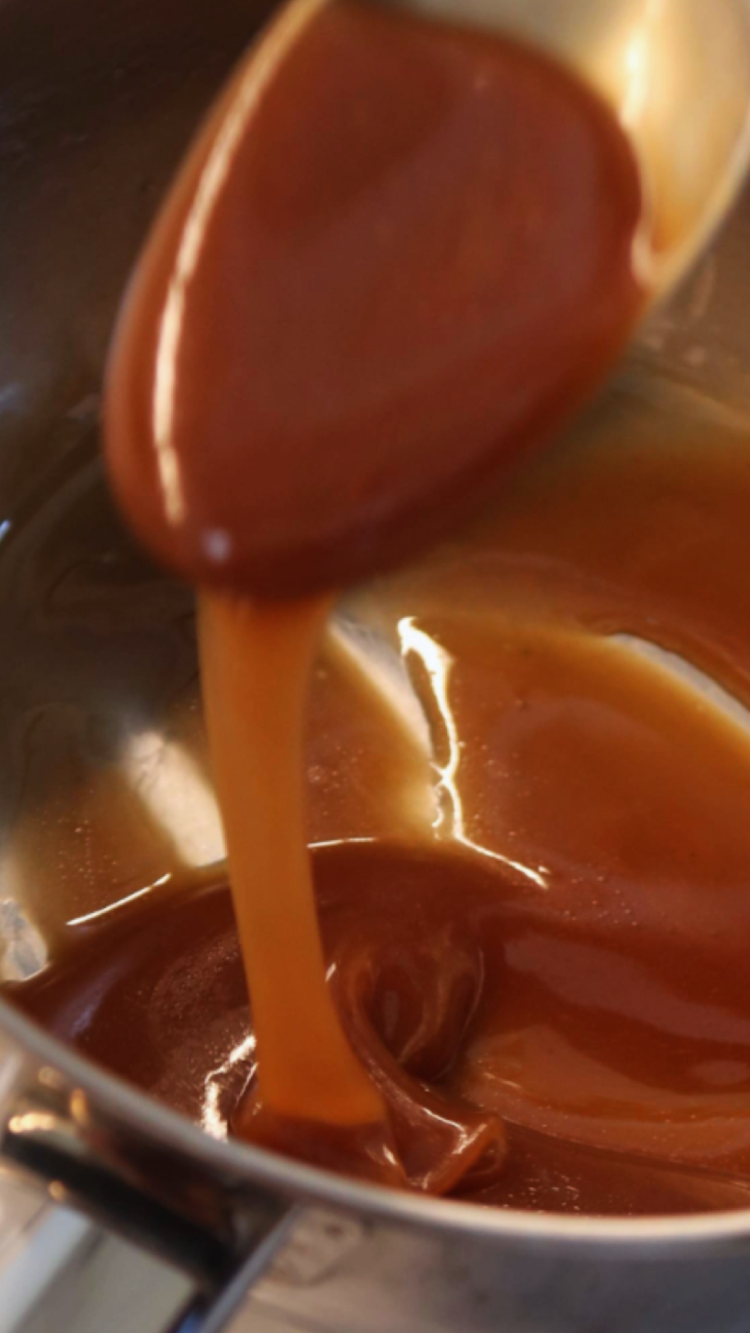 Pouring caramel sauce from a spoon into a pot of melted caramel.