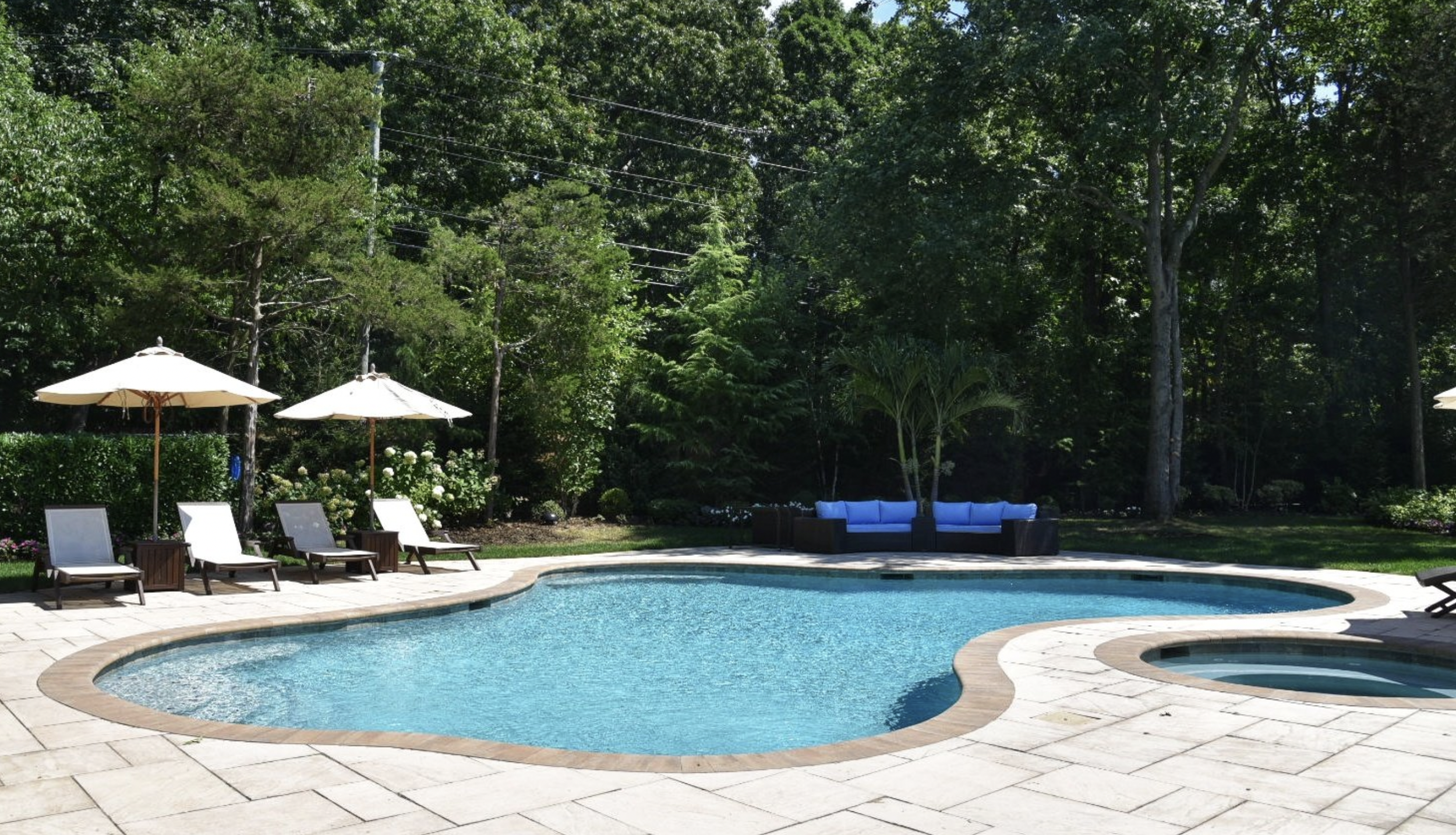 Backyard fiberglass pool with custom patio and landscaping in Port Jefferson, NY