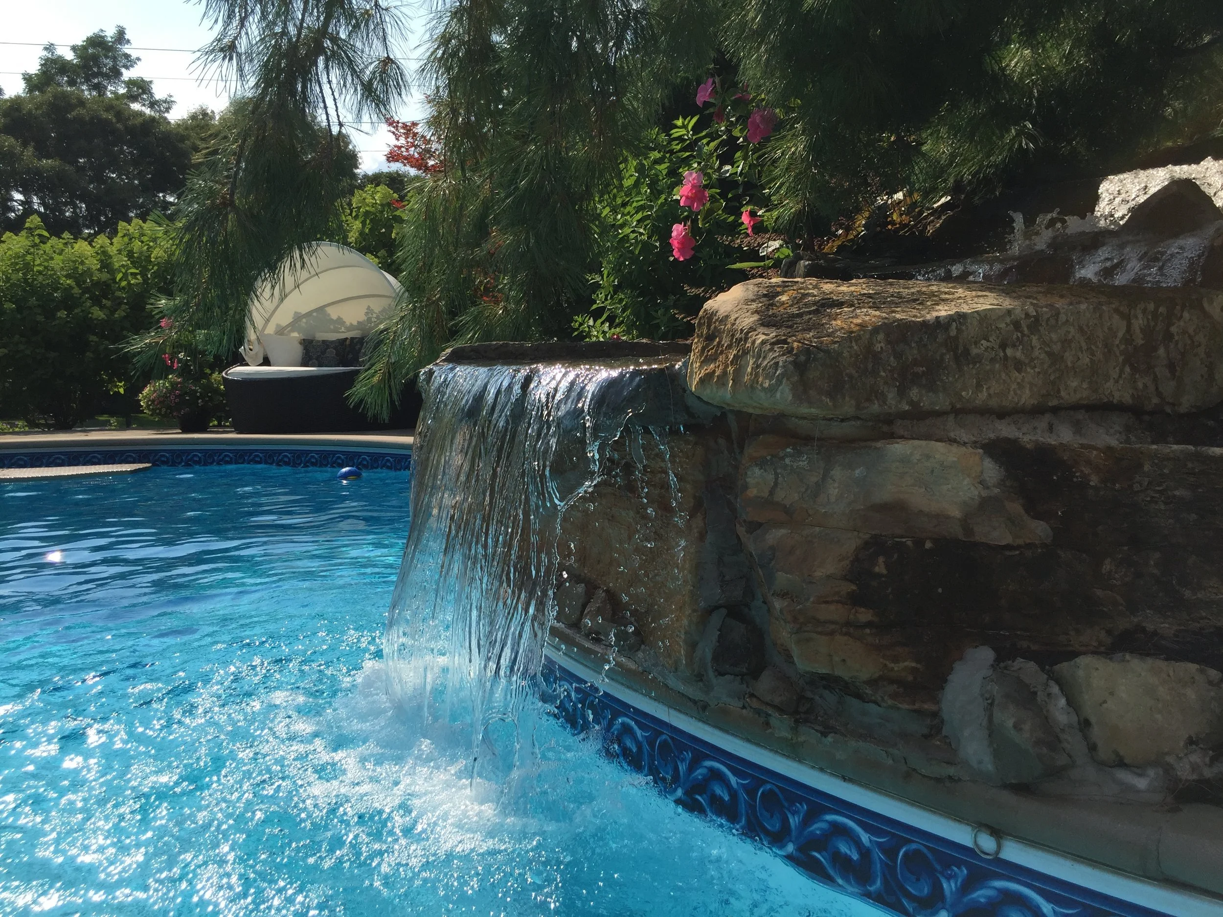 Multi-tier stone waterfall flowing into a landscaped pond in Miller Place, NY