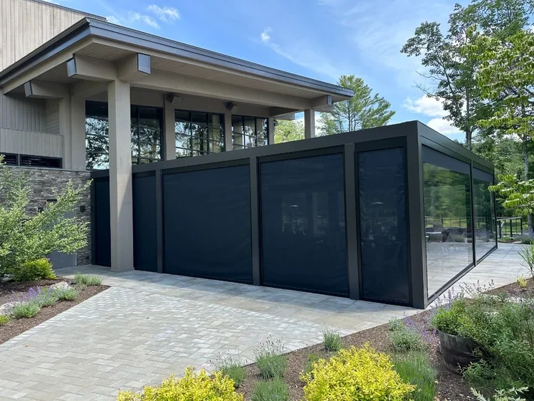 Modern house with an attached black glass sunroom or patio enclosure, surrounded by greenery and a paved walkway.